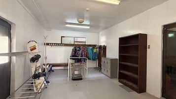 A hallway with a metal rack holding helmets and a bicycle, a clothing rack with colorful jackets, and a large cabinet with multiple drawers.
