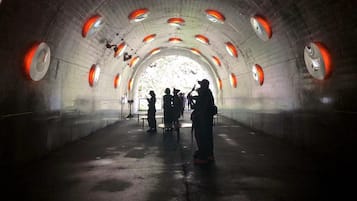 A tunnel with circular openings on the ceiling and a group of people standing at the end.