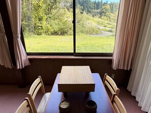 Une pièce avec une table et des chaises, une fenêtre avec des rideaux et une vue sur un espace verdoyant.