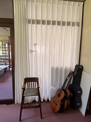 Une pièce avec une chaise en bois, une guitare et un étui à guitare, le tout adossé à un mur orné de rideaux légers.