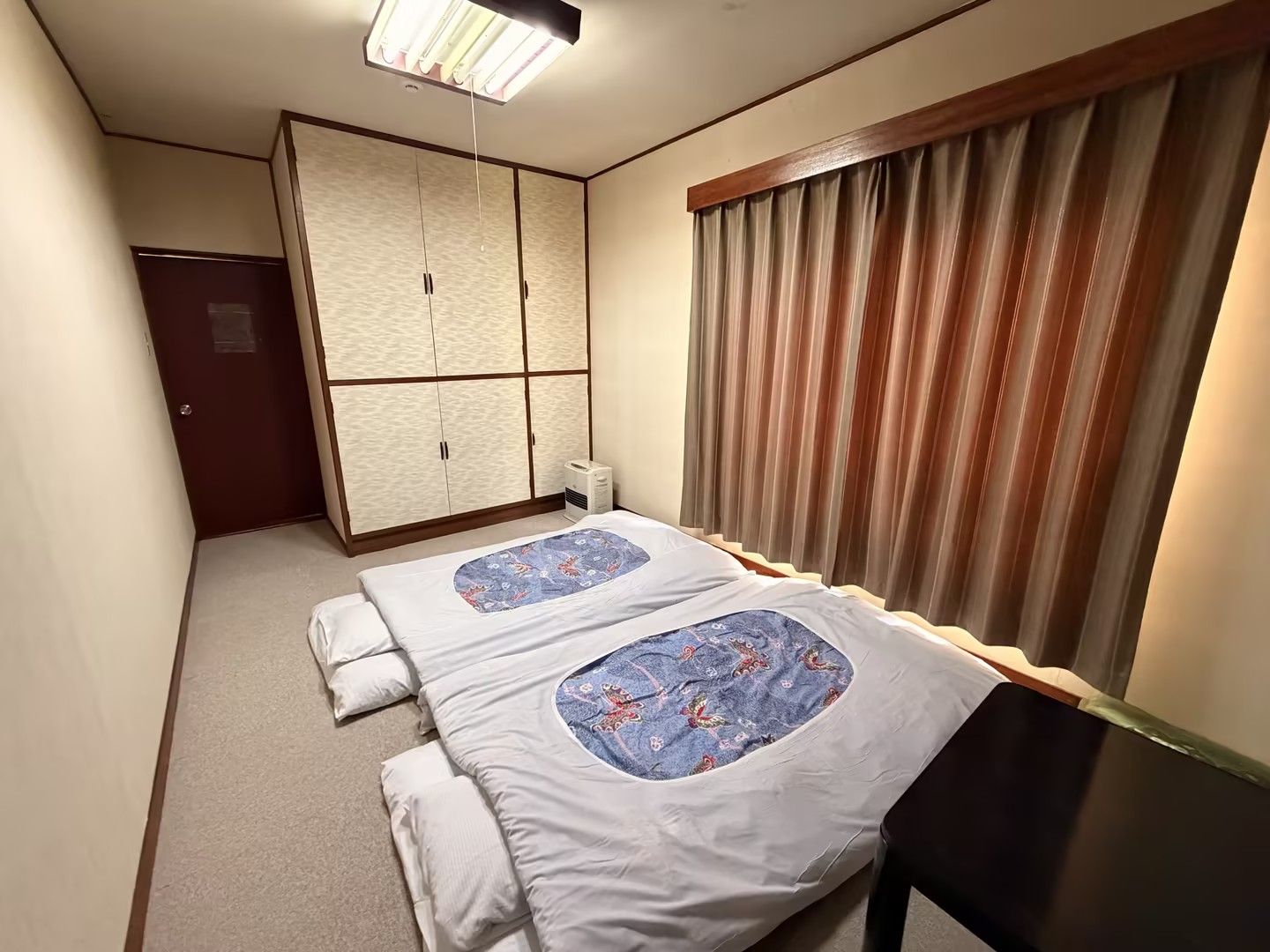 A hotel room with a bed, a wardrobe, a heater, and a window with curtains.