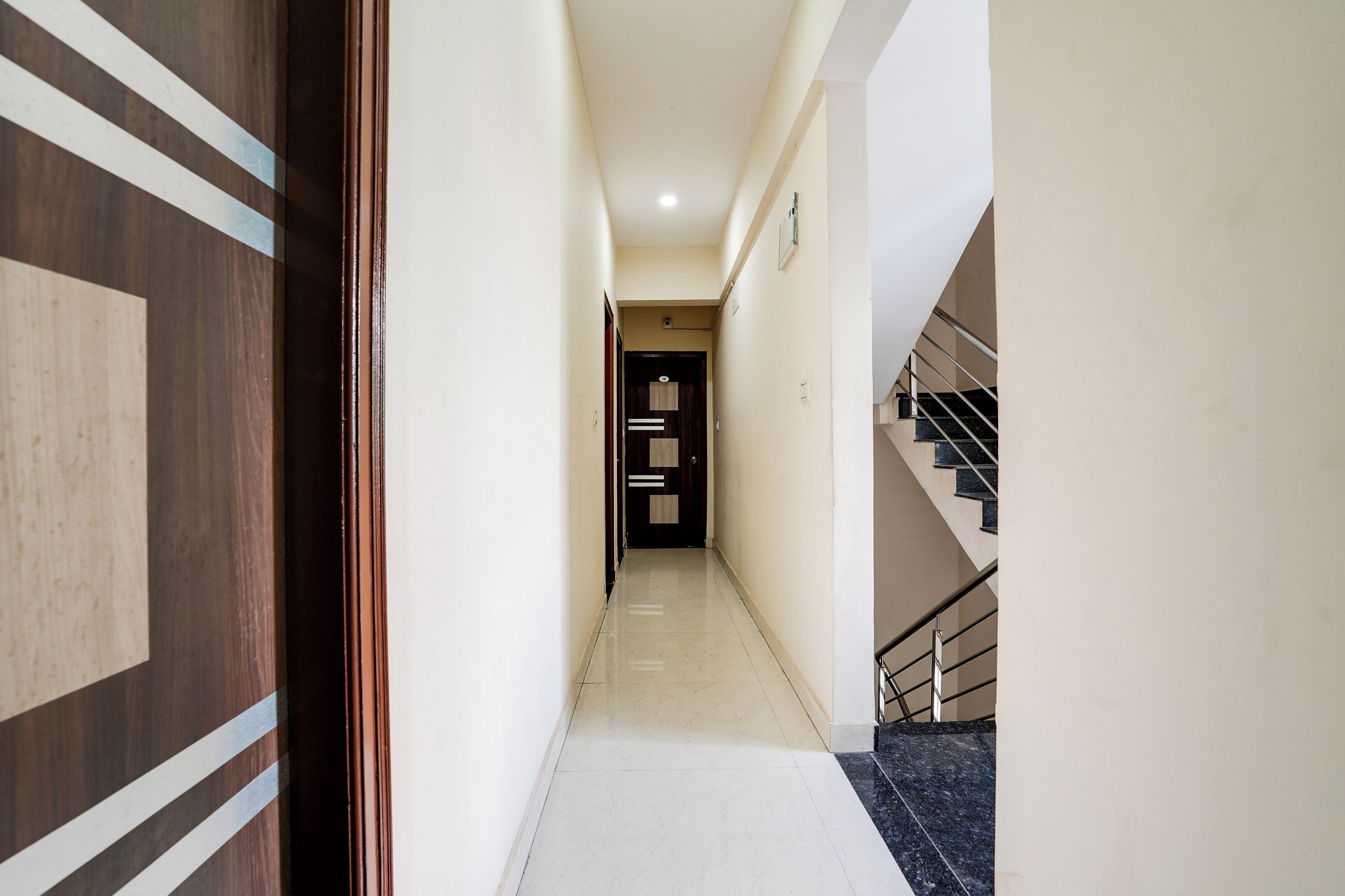 A corridor with a wooden door on the left, a staircase on the right, and a door at the end with a number plate.