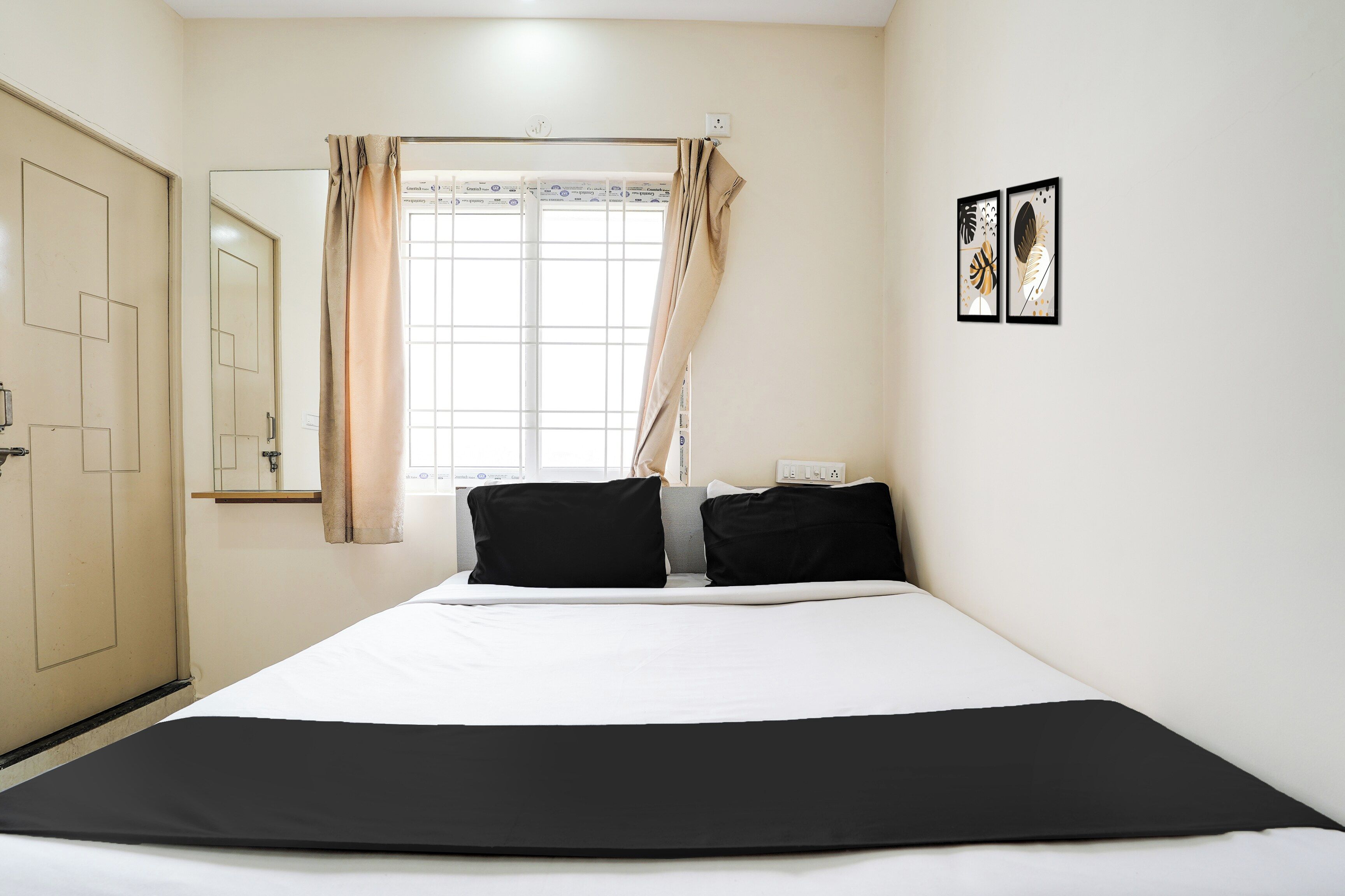 Une chambre d’hôtel avec un lit, une fenêtre avec des rideaux, une porte et une prise de courant fixée au mur.