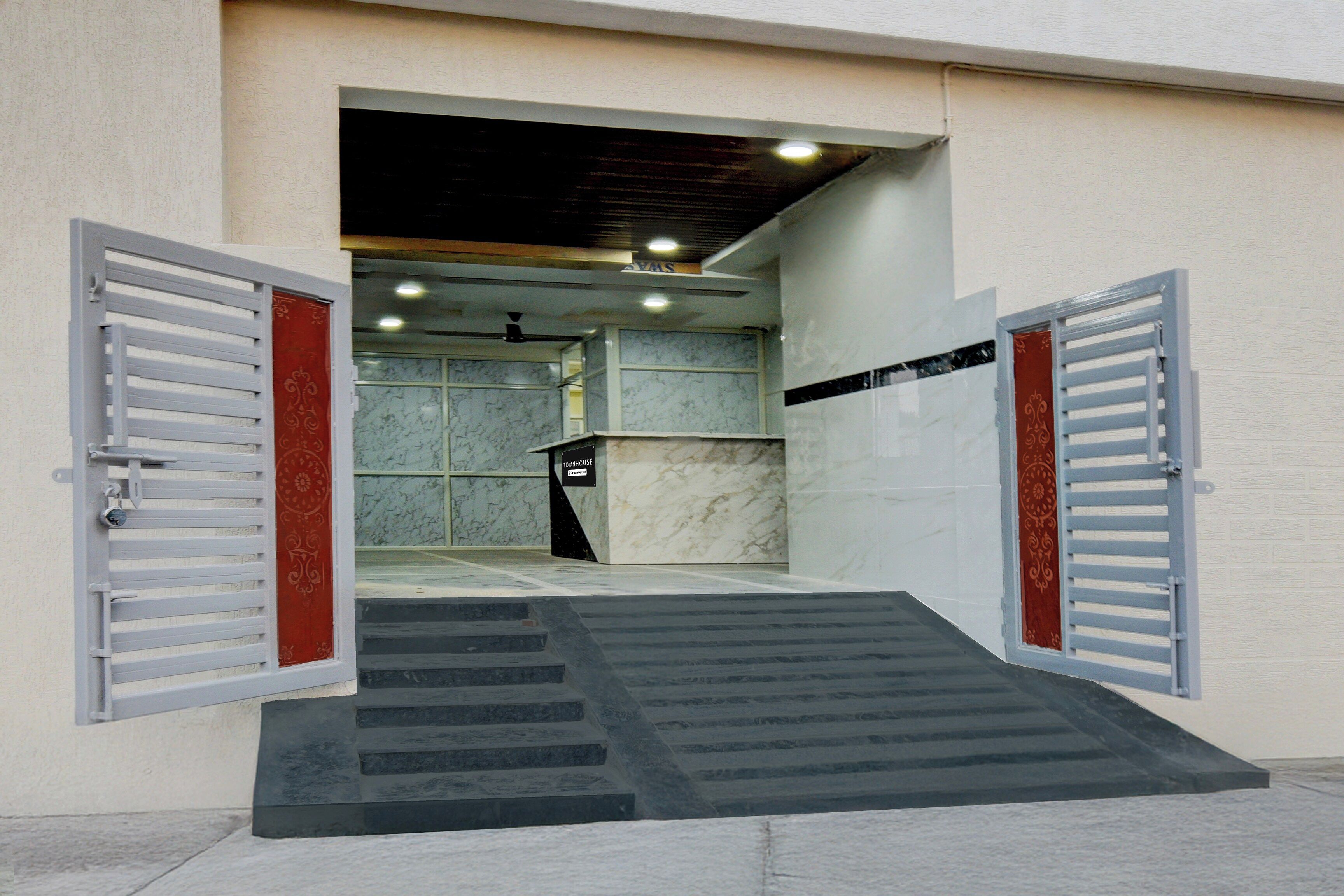 A building entrance with a ramp leading to a door, a sign reading 'TOWNHOUSE,' and a marble wall in the background.