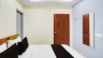 Quarto de hotel com cama, porta de madeira, cabideiro e espelho na parede.