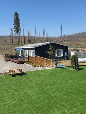A modern building with a deck and picnic table, surrounded by a well-maintained lawn and a forested area. - The Lassen Home, 3 bedrooms near Lake Almanor (Chester)
