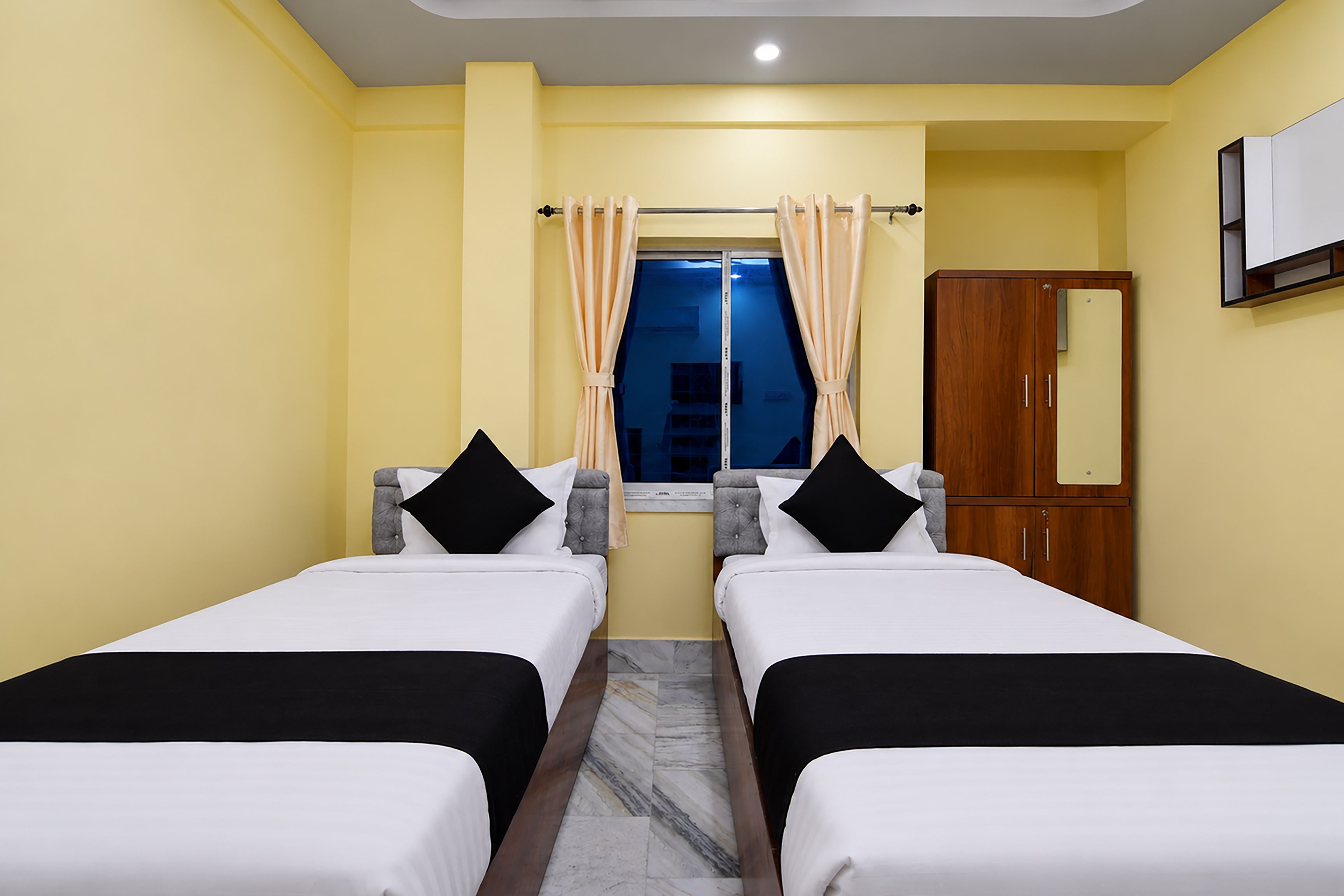 Habitación de hotel con dos camas, una ventana con cortinas, un armario y un espejo en la pared.