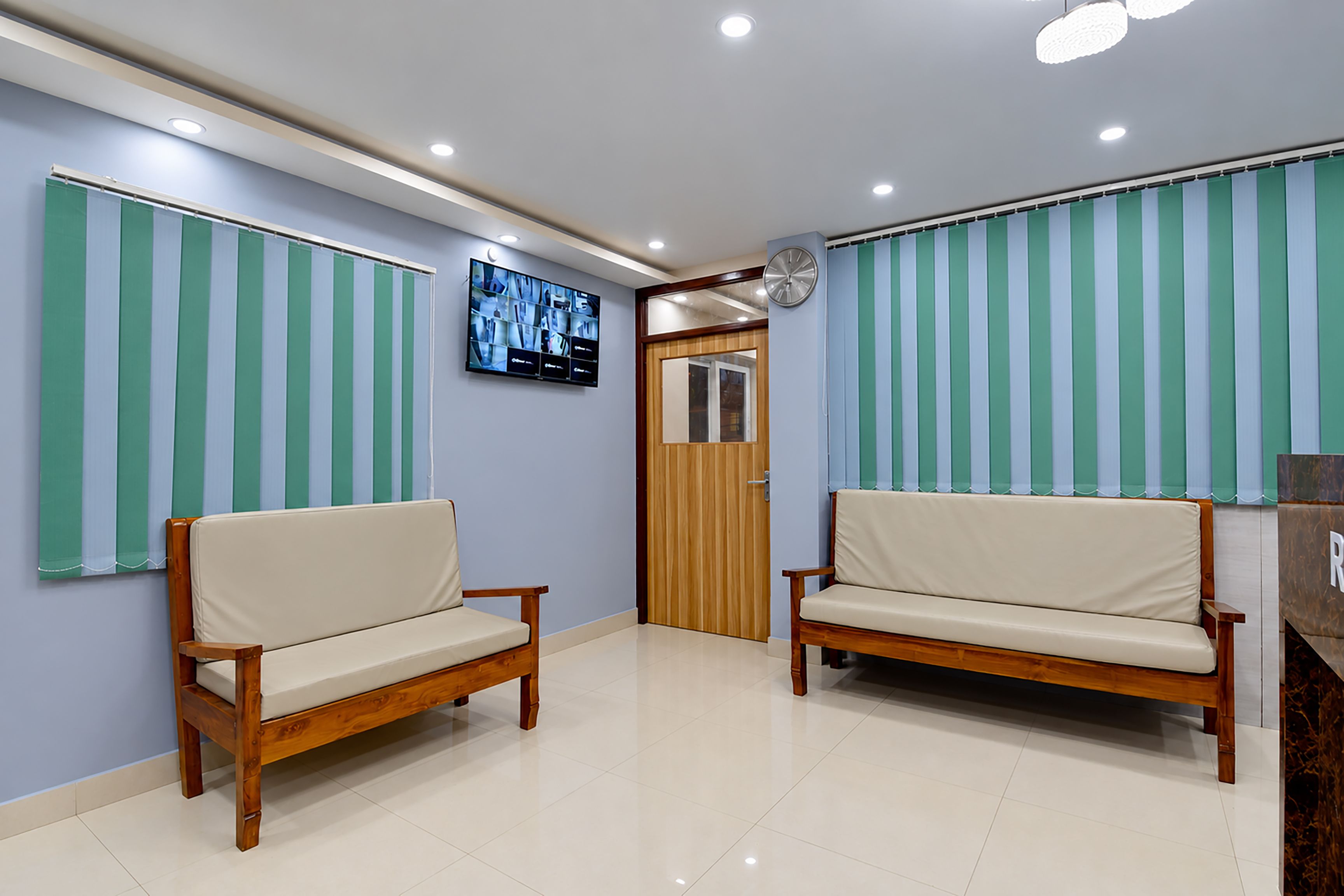 A reception area with two wooden sofas, a wall-mounted TV, and a clock.