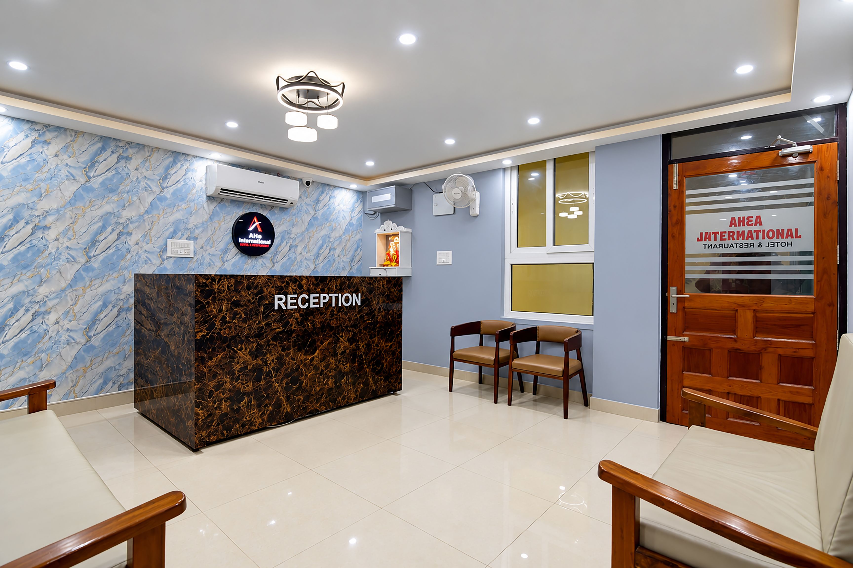 A reception area with a marble wall, a reception desk, a fan, and a door labeled 'AREA INTERNATIONAL HOTEL & RESORT'.