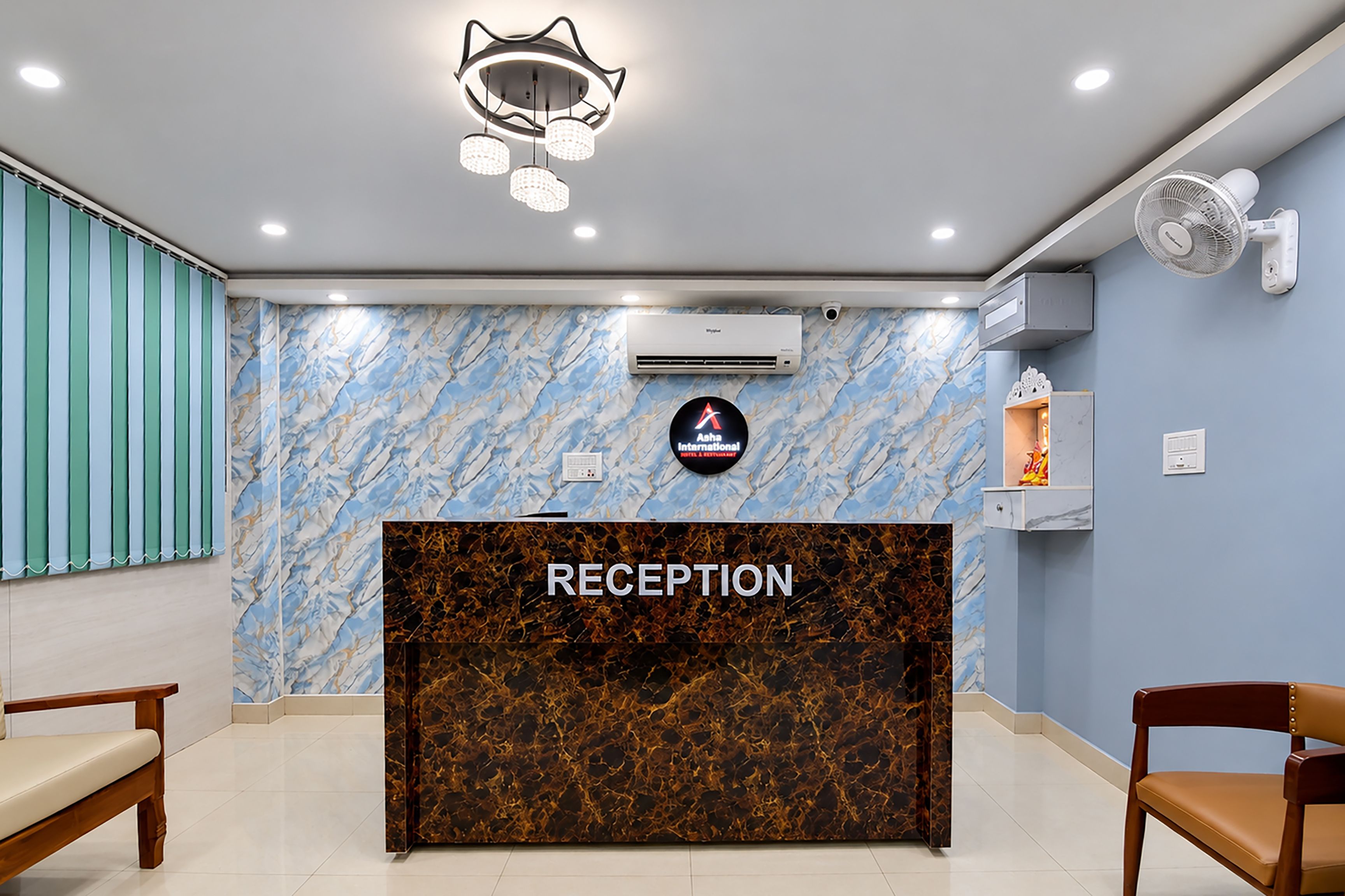 Un área de recepción con una pared de diseño de mármol, un mostrador de recepción con la etiqueta 'RECEPTION' y una unidad de aire acondicionado instalada en el techo.