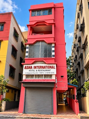 Un edifici de diversos pisos amb una façana vermella destacada, un rètol de 'Ash International Hotel & Restaurant' a la planta baixa i un persianes metàl·liques tancades.