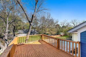 A wooden deck with a railing, surrounded by trees and a clear sky. - Jayhawk House - 5 min to KU/DWTN (Lawrence)