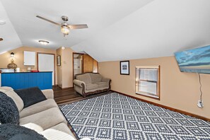 A living room with a sofa, a patterned rug, a ceiling fan, and a TV mounted on the wall. - Jayhawk House - 5 min to KU/DWTN (Lawrence)