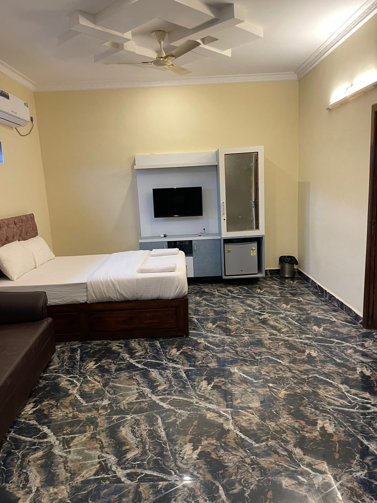 A hotel room with a bed, a TV, a ceiling fan, and a marble floor.