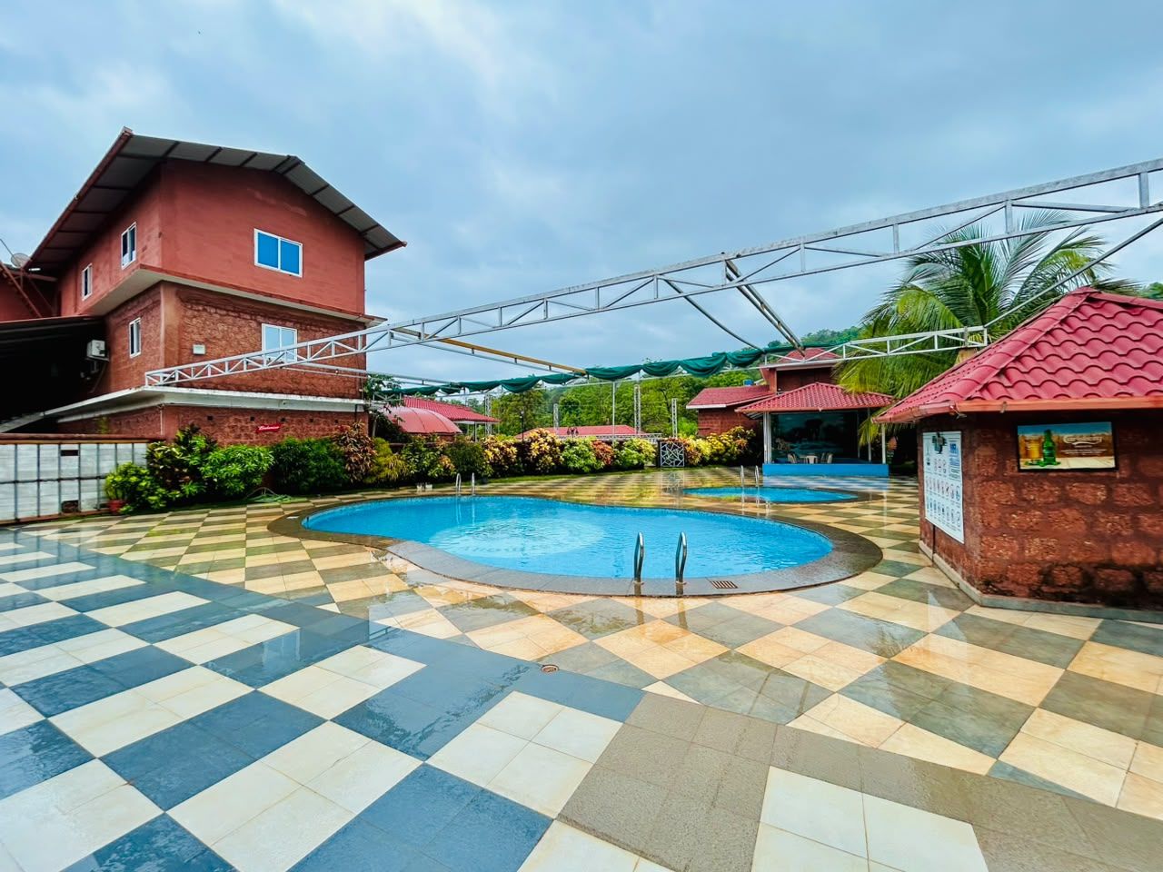 A swimming pool with a checkered floor, surrounded by buildings with red roofs and a covered walkway.