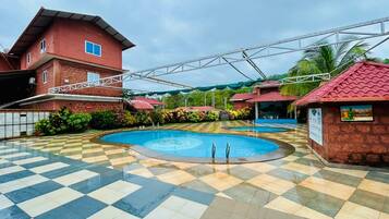 A swimming pool with a checkered floor, surrounded by buildings with red roofs and a covered walkway.