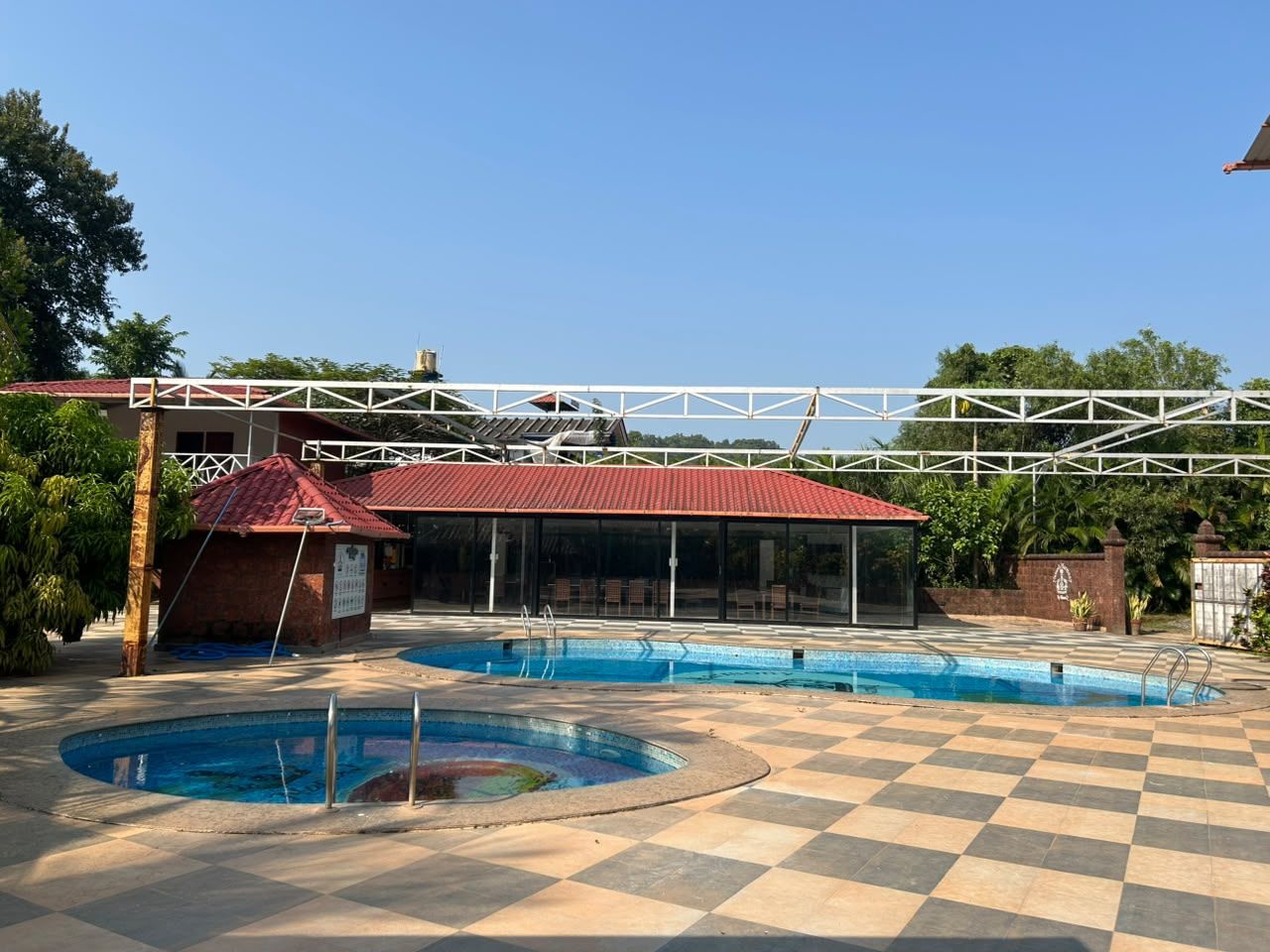 A pool area with a checkered floor, a covered seating area, and a small building with a red roof.