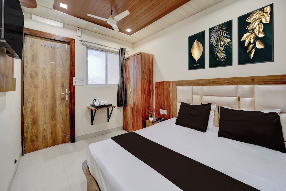 Ein Hotelzimmer mit Holztür, einem Bett mit weißer und schwarzer Bettwäsche, einem Nachttisch mit Telefon und einer Wand mit gerahmten Blätterbildern.