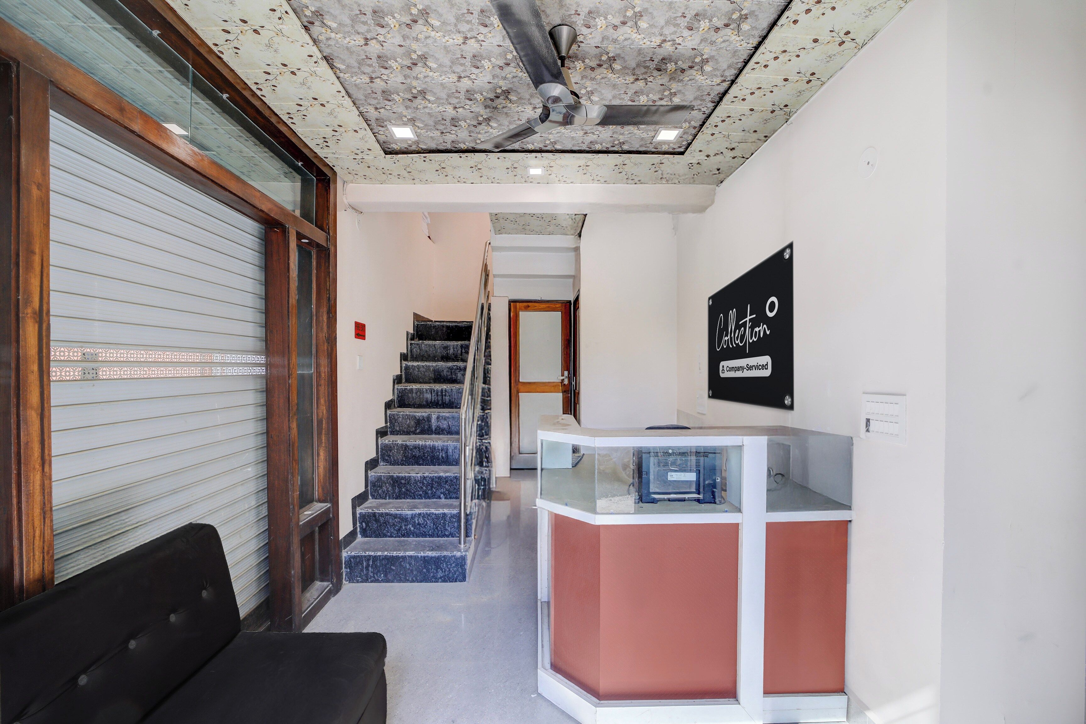 Zona de recepción de hotel con mostrador, escalera y una puerta con persiana cerrada.
