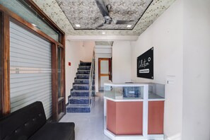 Zona de recepción de hotel con mostrador, escalera y una puerta con persiana cerrada.