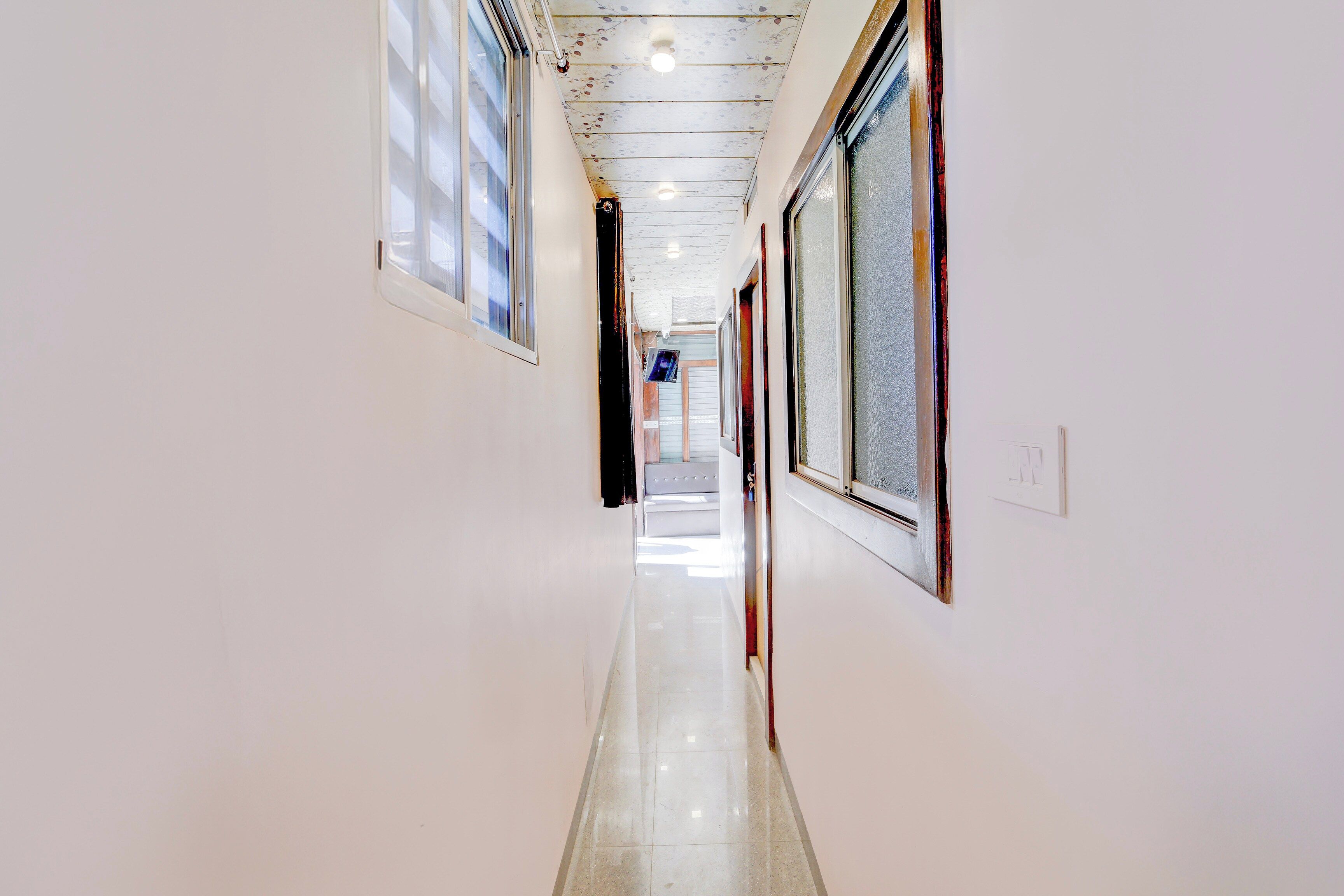 Corredor com paredes brancas e piso ladrilhado, que leva a um quarto com porta.