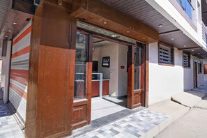 Entrada de un edificio con una puerta metálica enrollable, un cartel que indica punto de recogida y un pavimento adoquinado que lleva a la entrada.