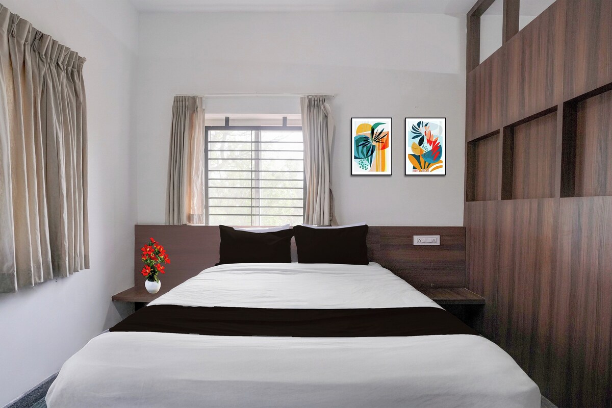A hotel room with a bed, a nightstand, a vase of flowers, and two abstract paintings on the wall.