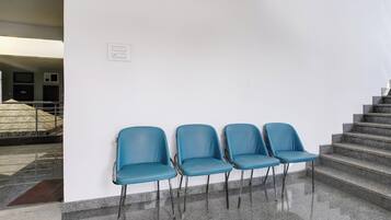A set of four blue chairs against a white wall, positioned on a polished stone floor with a staircase to the right.
