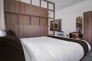 A hotel room with a large bed, a wooden headboard, a desk with a chair, a mirror, and a wardrobe.