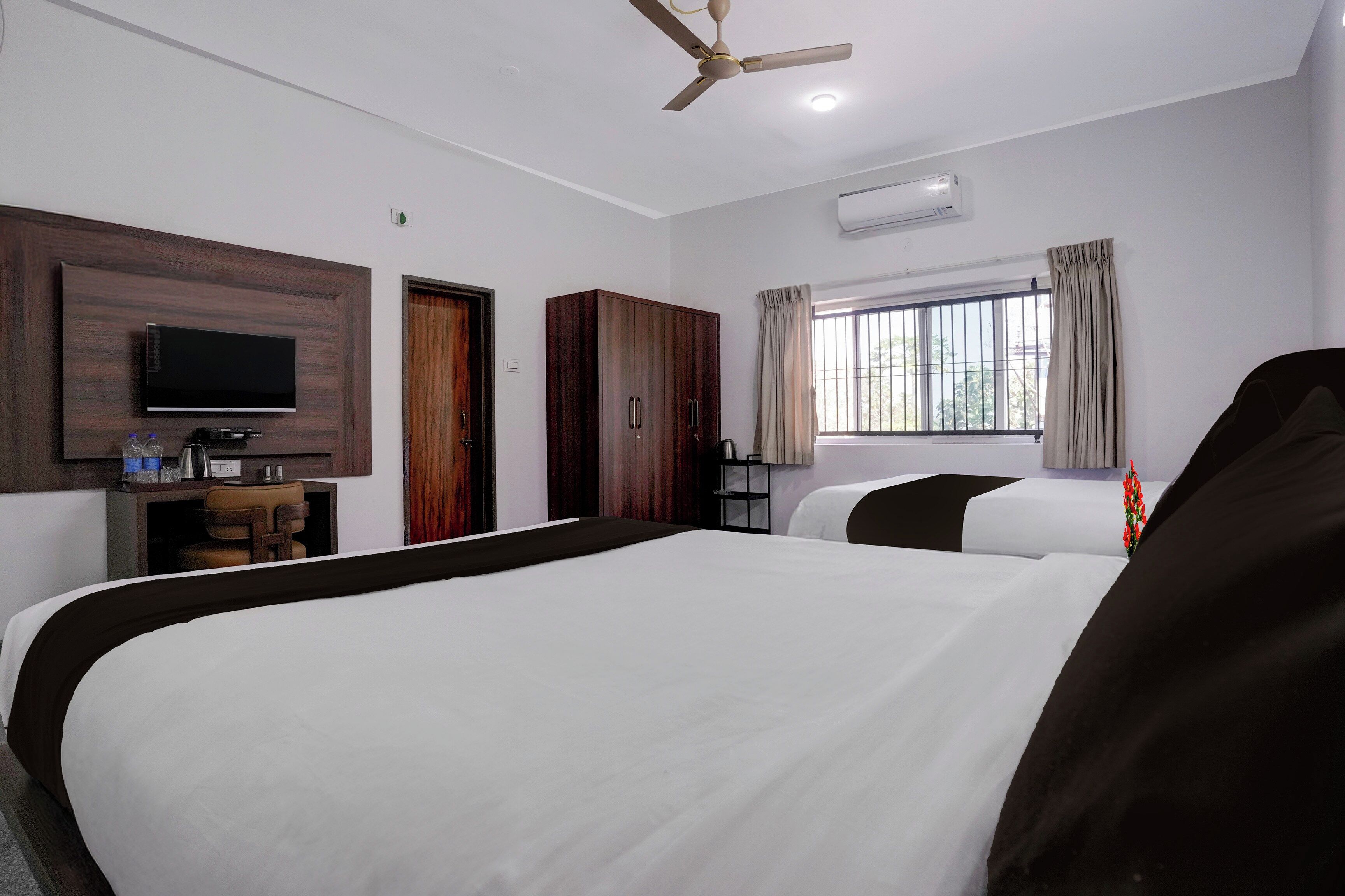 A hotel room with a large bed, a television, a wardrobe, a desk, and a window with curtains.