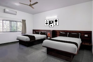 Habitación de hotel con dos camas, ventilador de techo, unidad de aire acondicionado, ventana con rejas y decoración en la pared.