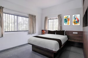 Un dormitorio moderno con una cama grande, dos ventanas con cortinas y dos cuadros abstractos en la pared.