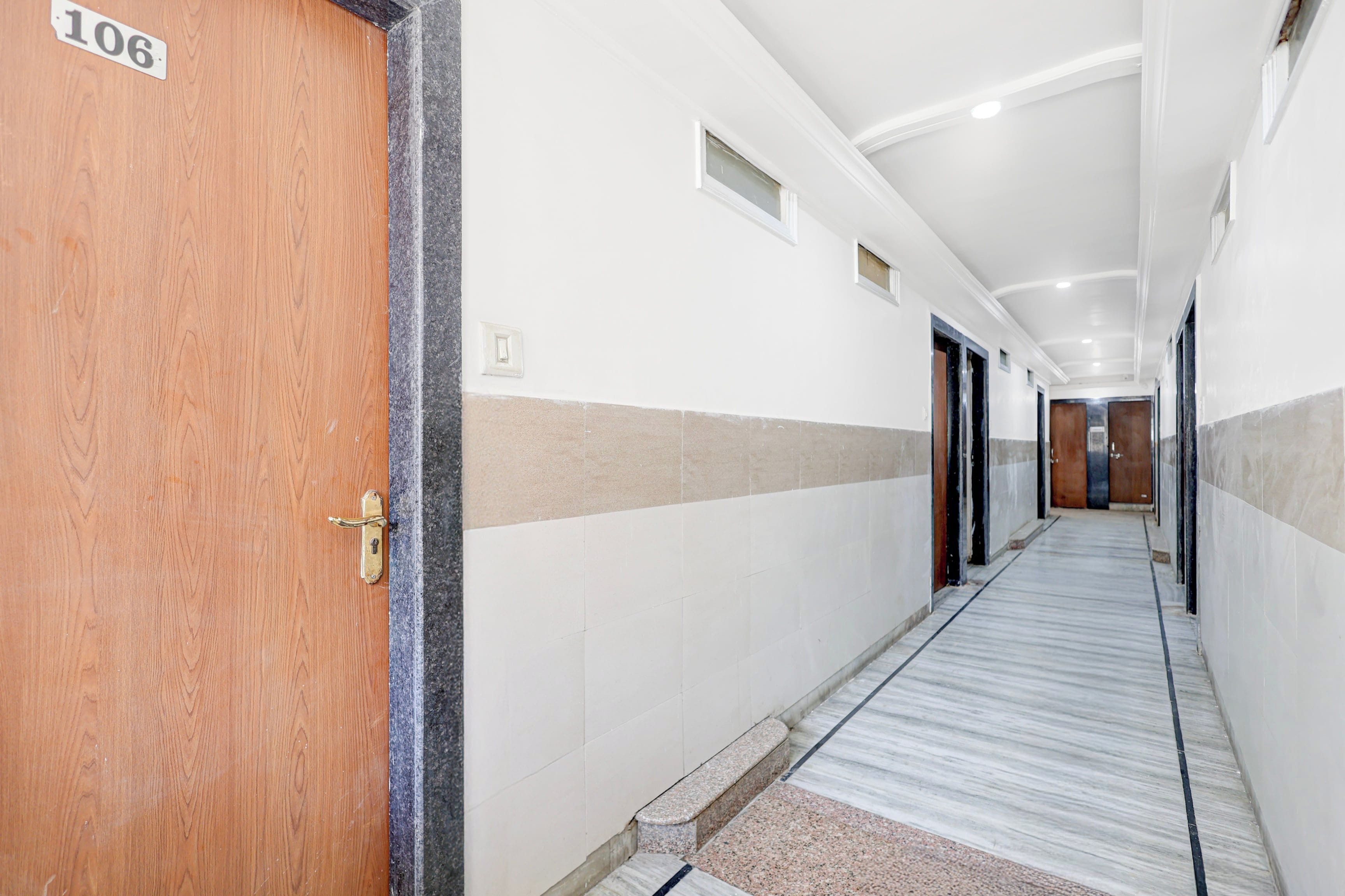 Pasillo de hotel con puerta de madera identificada con el número 106, paredes con azulejos y suelo de mármol.