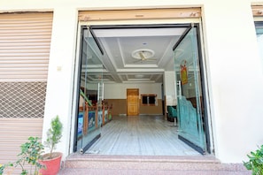 Entrada de hotel con puerta de vidrio, una puerta de madera en el interior y un pequeño ventanal en la pared.