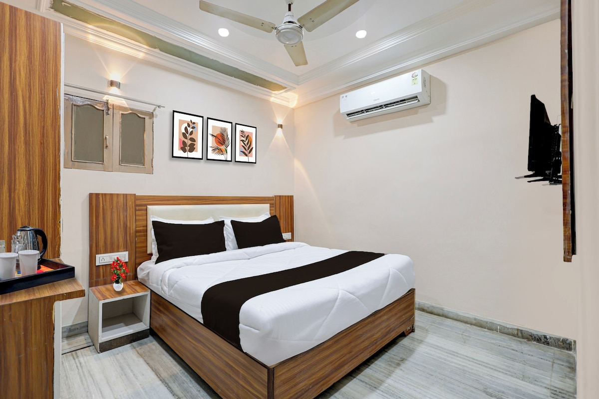 Habitación de hotel con cama de madera, mesita de noche, espejo, aire acondicionado instalado en la pared y cuadros enmarcados.
