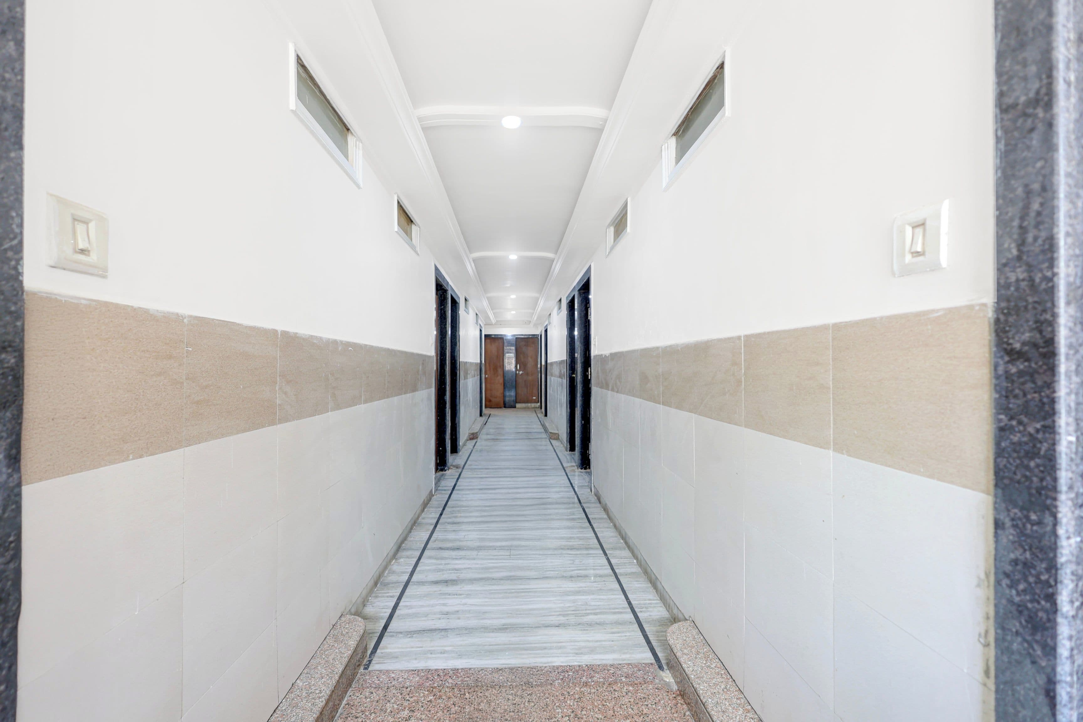 Un largo pasillo estrecho con paredes blancas y piso de mármol, que conduce a una puerta al final.