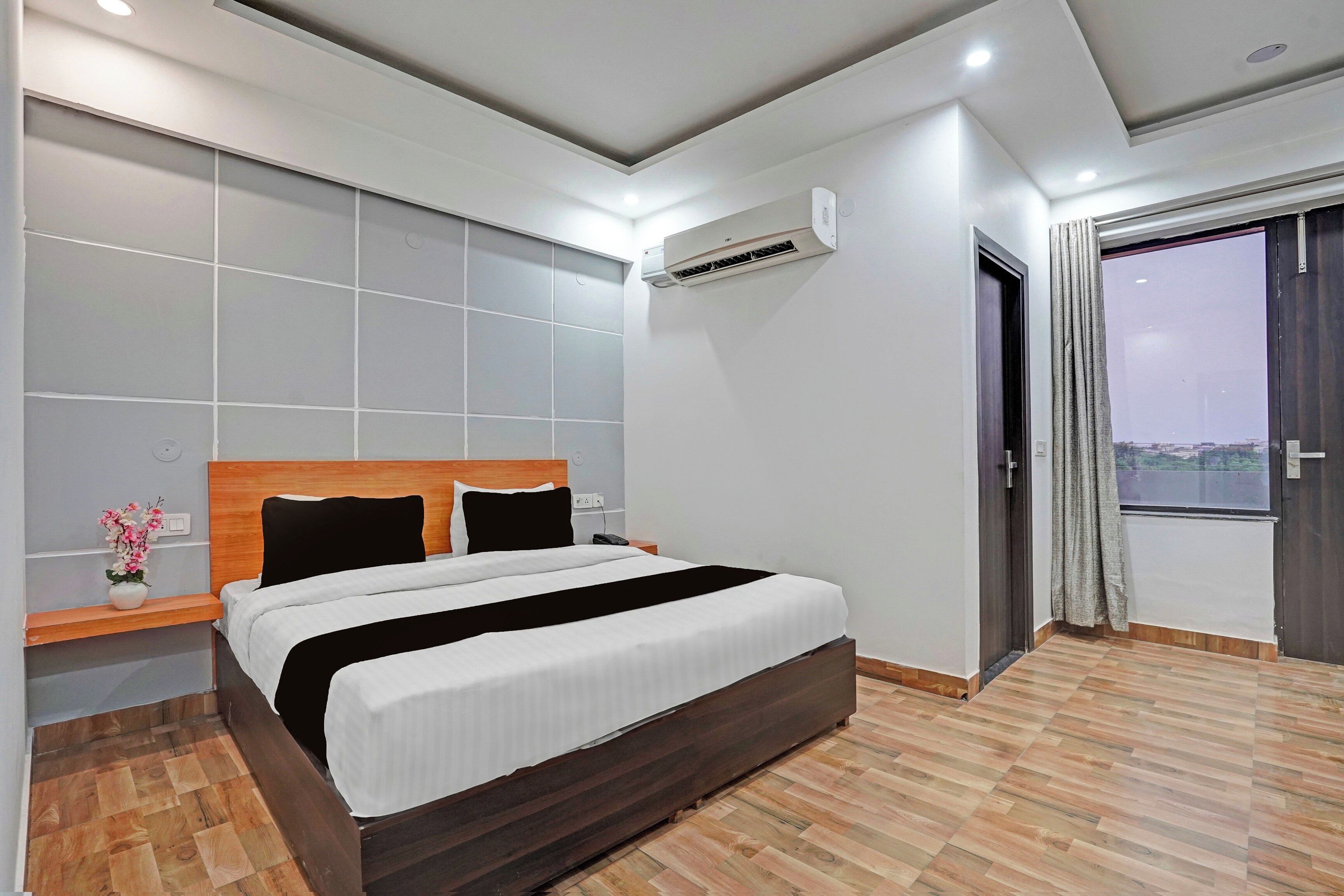 Habitación de hotel moderna con una cama grande, una mesita de noche, un equipo de aire acondicionado y vistas a través de una puerta.