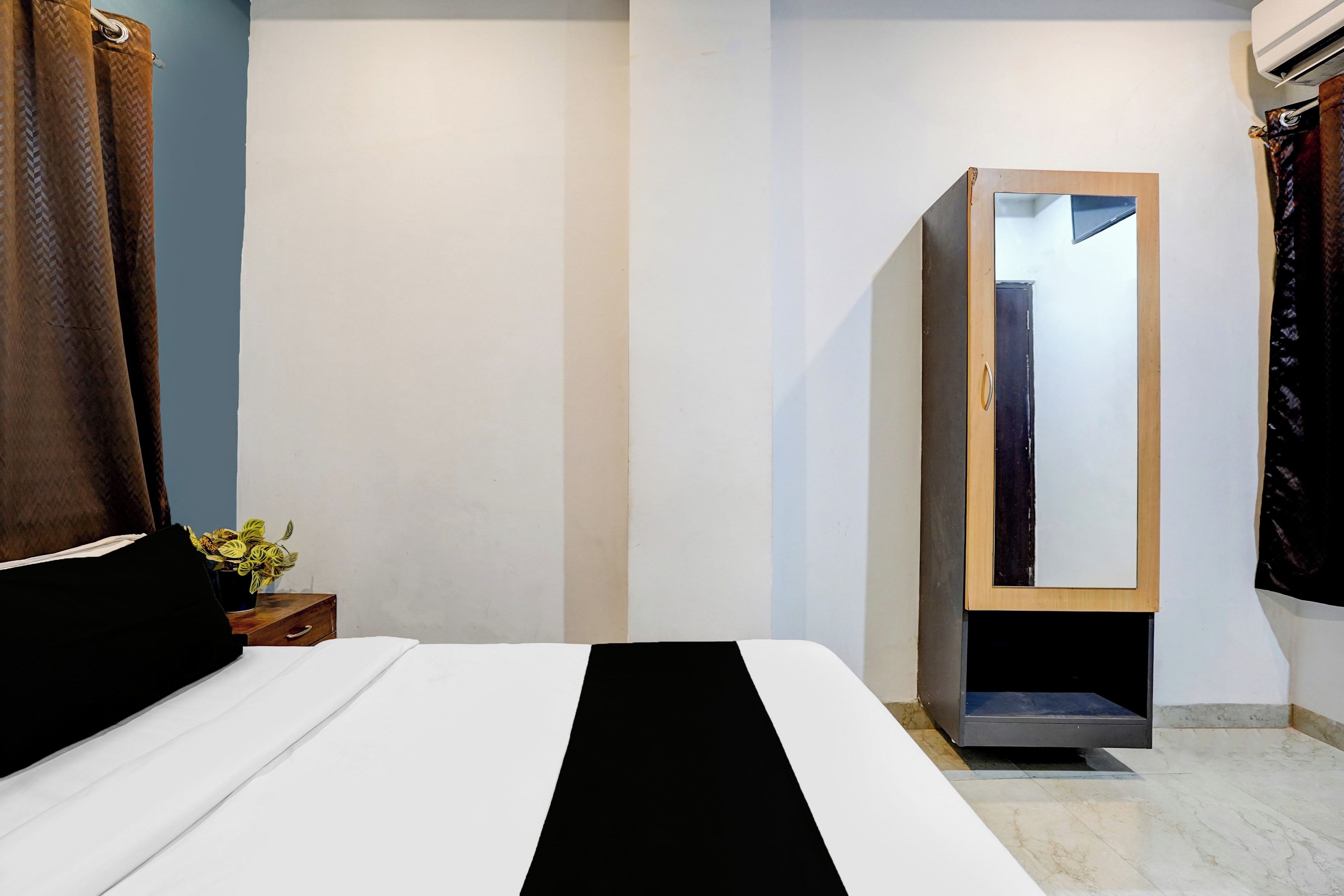Une chambre d’hôtel avec un lit, une armoire, un miroir et une petite table sur laquelle est posée une plante.