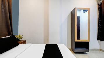 A hotel room with a bed, a wardrobe, a mirror, and a small table with a plant.