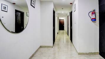 A corridor with a round mirror, framed pictures, a fire extinguisher, and a door at the end.