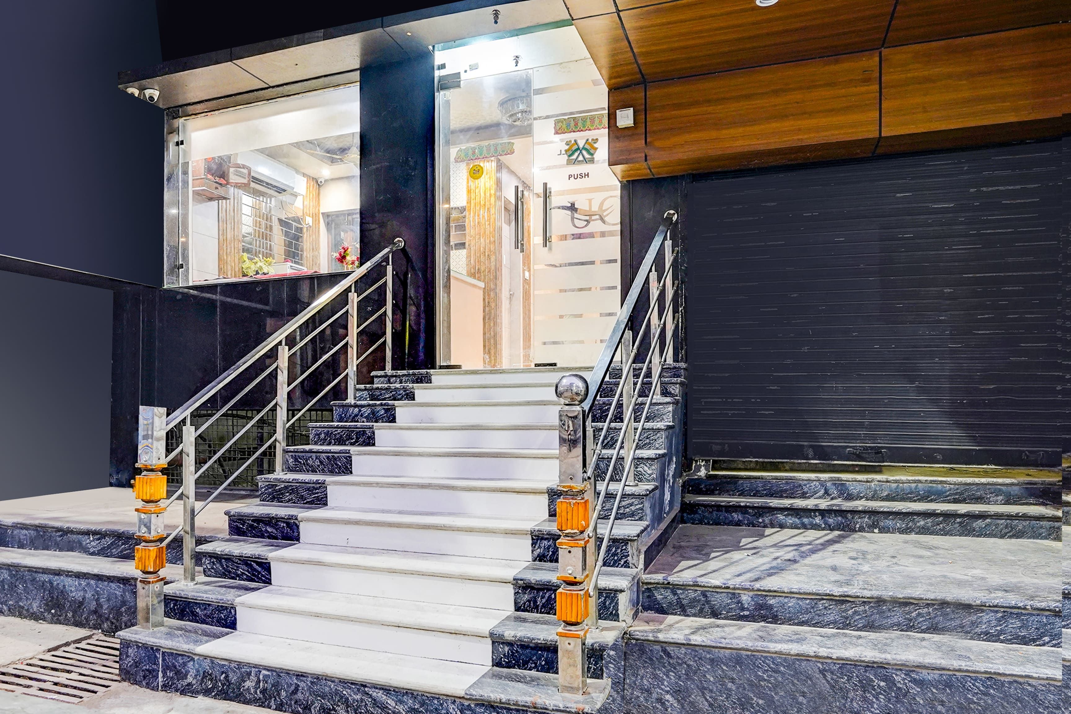 Una escalera con escalones de mármol y barandillas de metal, que conduce a una entrada con puertas de vidrio y una barra de empuje.