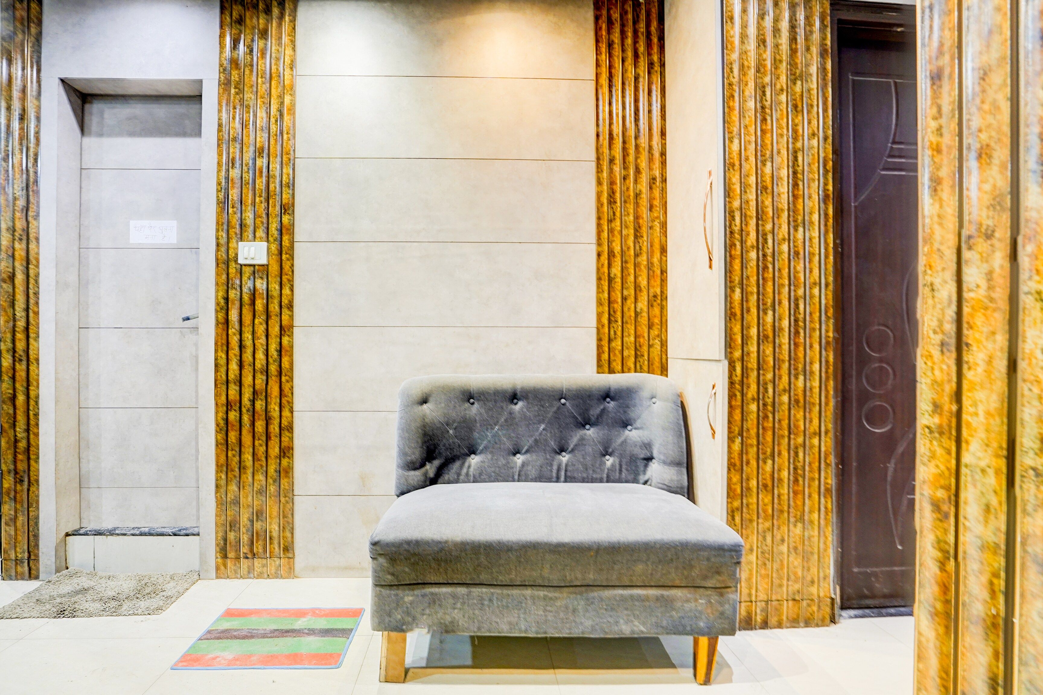 A room with a grey upholstered chair, a marble wall, and a door with a golden pattern.