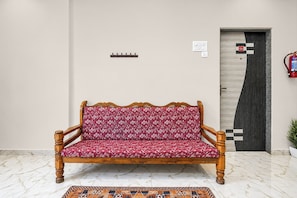 A wooden sofa with a floral pattern, a tiled floor, a door with a checkered pattern, and a fire extinguisher mounted on the wall. - Townhouse Lingmala Waterfall (Mahabaleshwar)