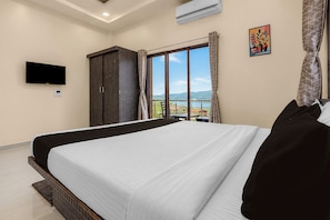 A hotel room with a large bed, a flat-screen TV, an air conditioner, a window with a view of the mountains, and a painting on the wall. - Townhouse Lingmala Waterfall (Mahabaleshwar)