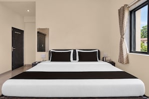 A hotel room with a large bed, a nightstand, a telephone, and a window with curtains. - Townhouse Lingmala Waterfall (Mahabaleshwar)