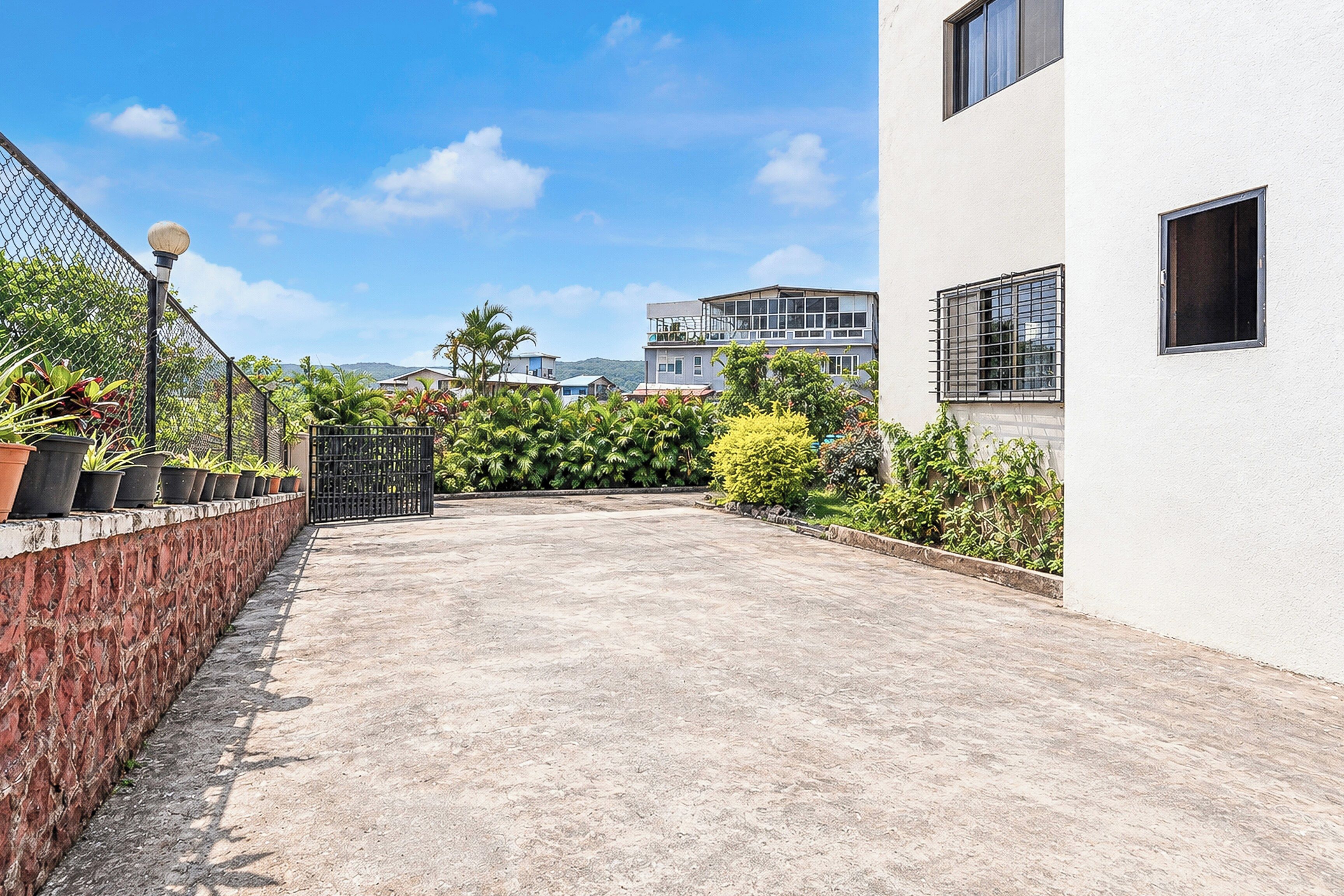 A paved courtyard with a brick wall, potted plants, and a metal gate.