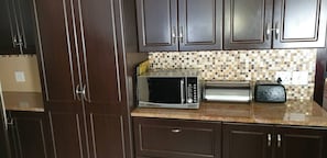 A kitchen with dark wooden cabinets, a tiled backsplash, a microwave, a toaster, and a countertop. - Stellenbosch Holiday Home (Stellenbosch)