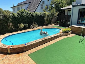 A rectangular swimming pool with a brick edge, surrounded by a green artificial turf area and a brick patio. - Stellenbosch Holiday Home (Stellenbosch)