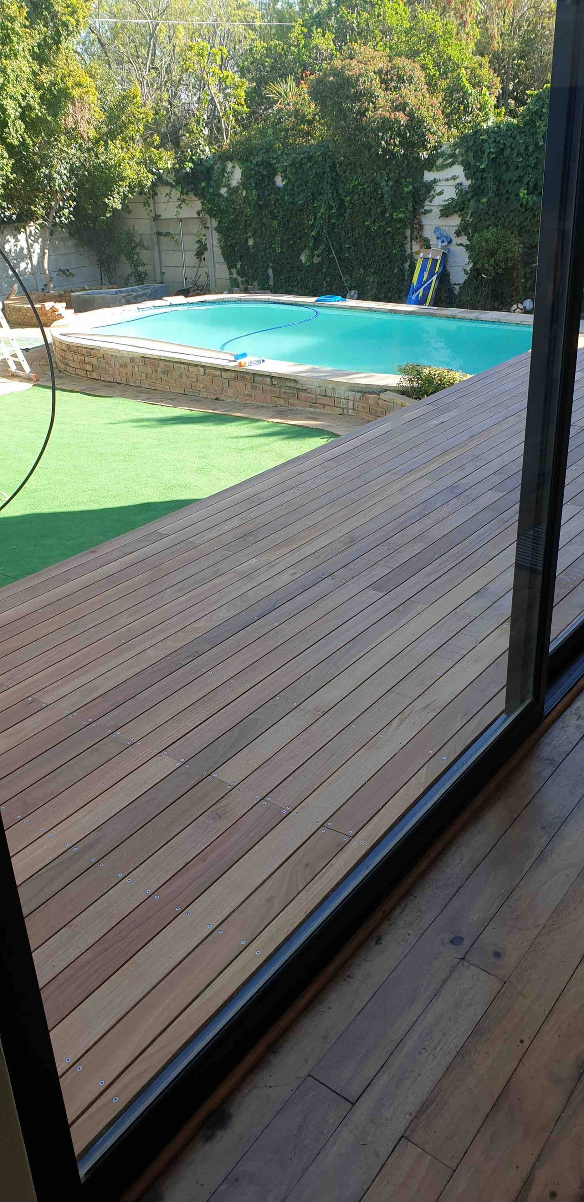 Une terrasse en bois avec une piscine et un espace recouvert d’un gazon synthétique vert.
