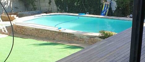 A wooden deck with a pool and a green artificial turf area.